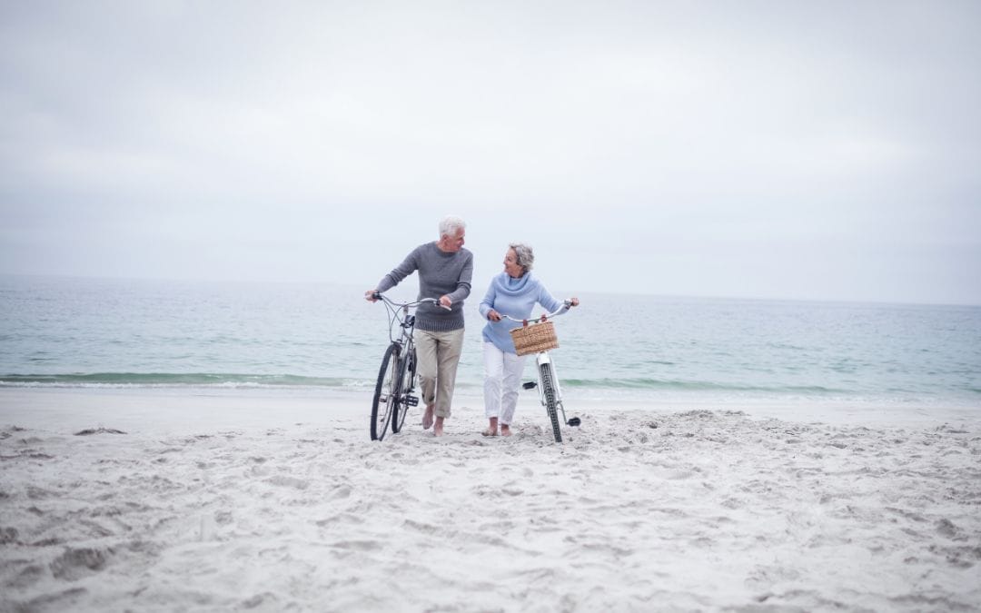 Senior couple walking on beach with bikes