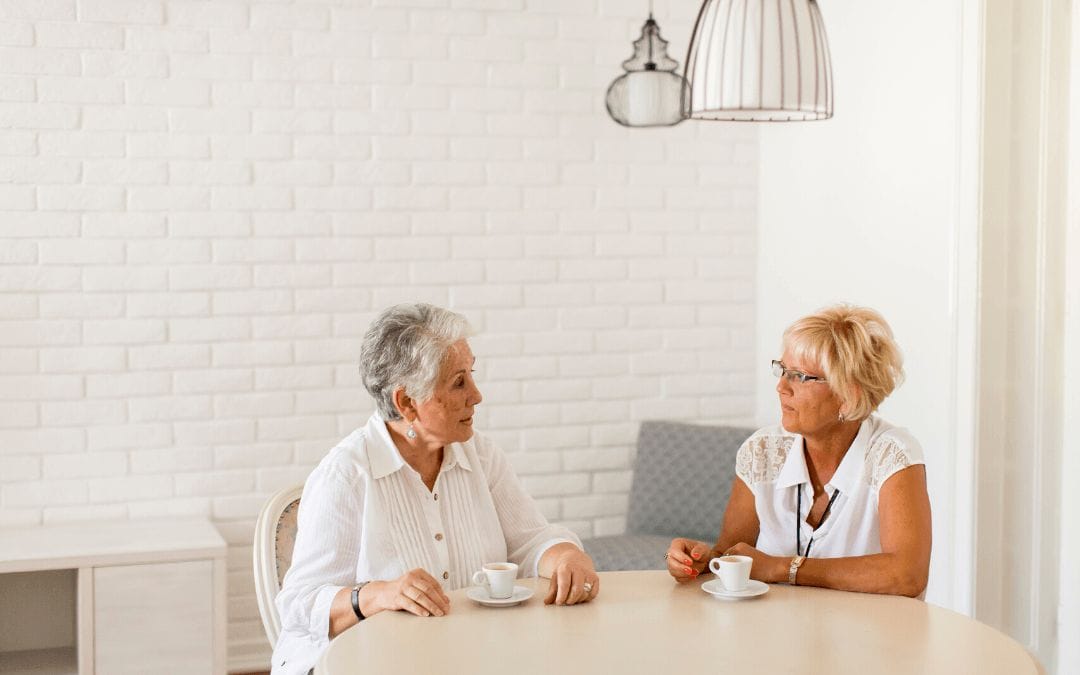 Elderly mother and daughter sitting at table having coffee together