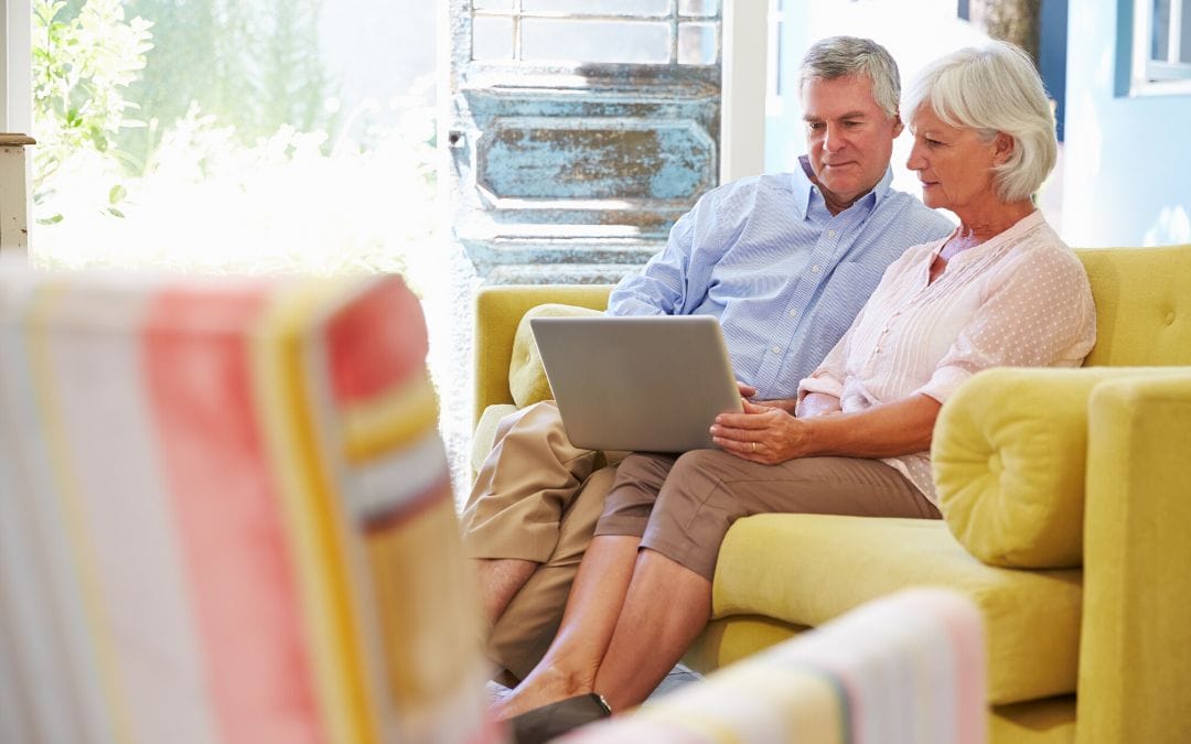 Elderly couple sitting on couch using laptop together