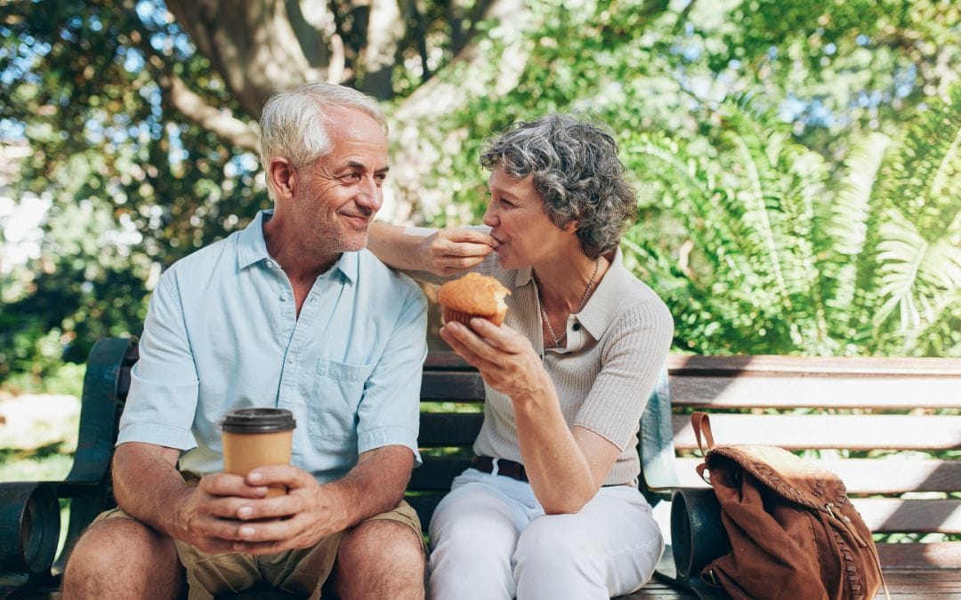 Elderly couple sitting together outside on park bench eating